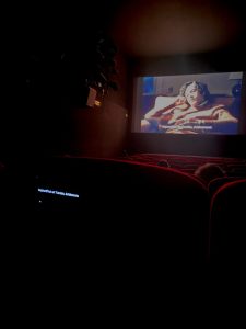 Interieur du cinéma avec film à l'écran et sous-titres sur téléphone scratché au siège.