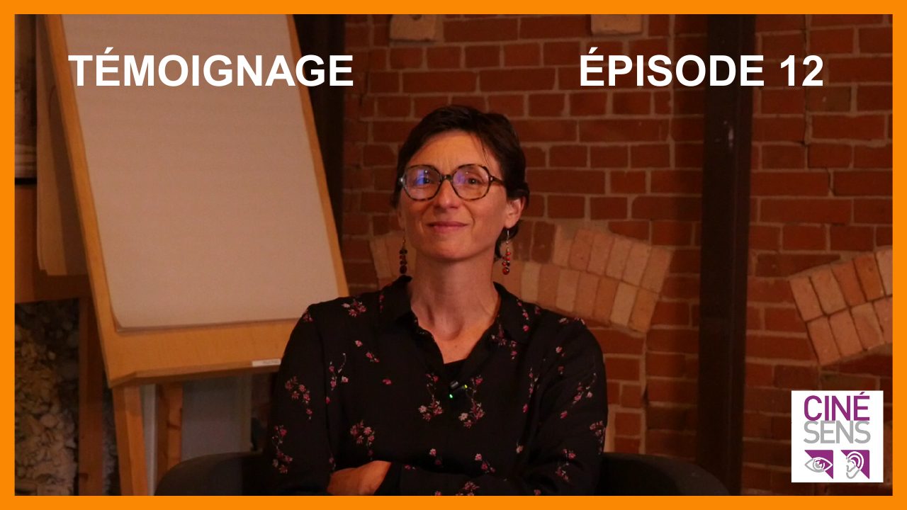 Caroline, cheveux courts, lunettes rondes se tient assise, les bras croisés, devant un mur de briques rouges.