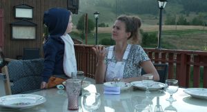 On voit une jeune femme et un enfant à table à l'extérieur dans un chalet de montagne