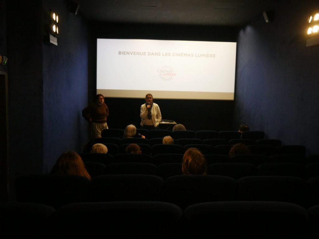 Cécile Dumas, de Ciné Sens face à une salle de cinéma plongée dans l'obscurité pour présenter la démonstration d'une séance inclusive.