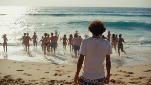 Un homme regarde de dos la plage et la mer, des gens courent vers l'eau